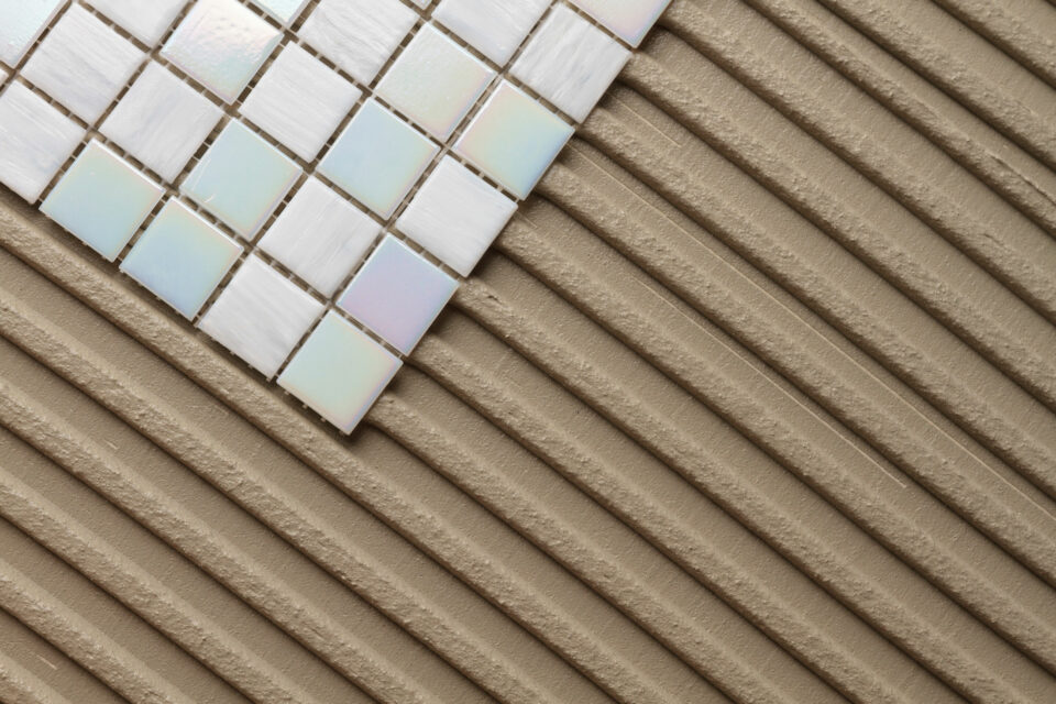 A floor is being tiled in the bathroom, you can see mosaic tiles and tile adhesive